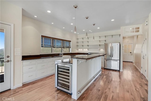 kitchen featuring freestanding refrigerator, wine cooler, a kitchen island, dark countertops, and light wood-style floors