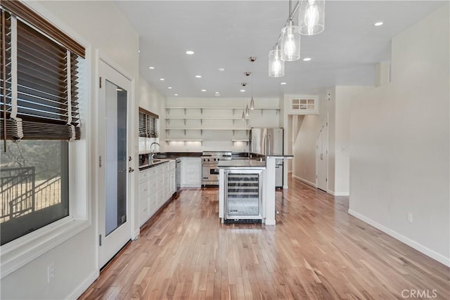 kitchen with sink, appliances with stainless steel finishes, white cabinetry, decorative light fixtures, and light wood-type flooring