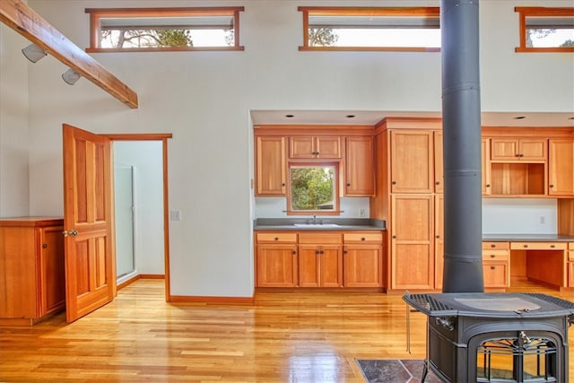 kitchen with sink, light hardwood / wood-style floors, a high ceiling, and a wood stove