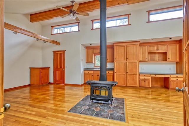 kitchen with light hardwood / wood-style flooring, ceiling fan, beam ceiling, built in desk, and a wood stove