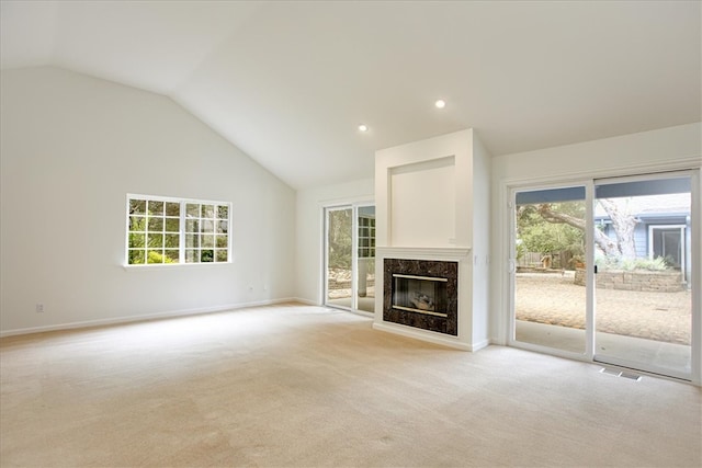 unfurnished living room featuring a premium fireplace, plenty of natural light, light colored carpet, and high vaulted ceiling