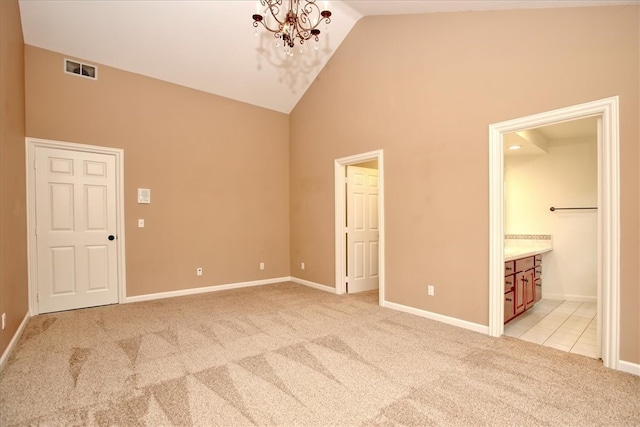 unfurnished bedroom featuring light carpet, a notable chandelier, connected bathroom, and high vaulted ceiling