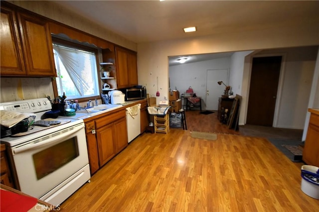 kitchen with light wood finished floors, white appliances, brown cabinetry, and a sink