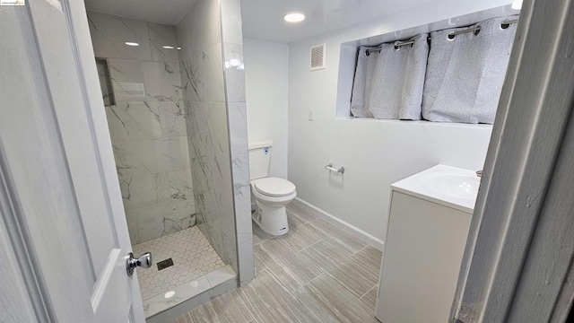 bathroom featuring vanity, a tile shower, and toilet