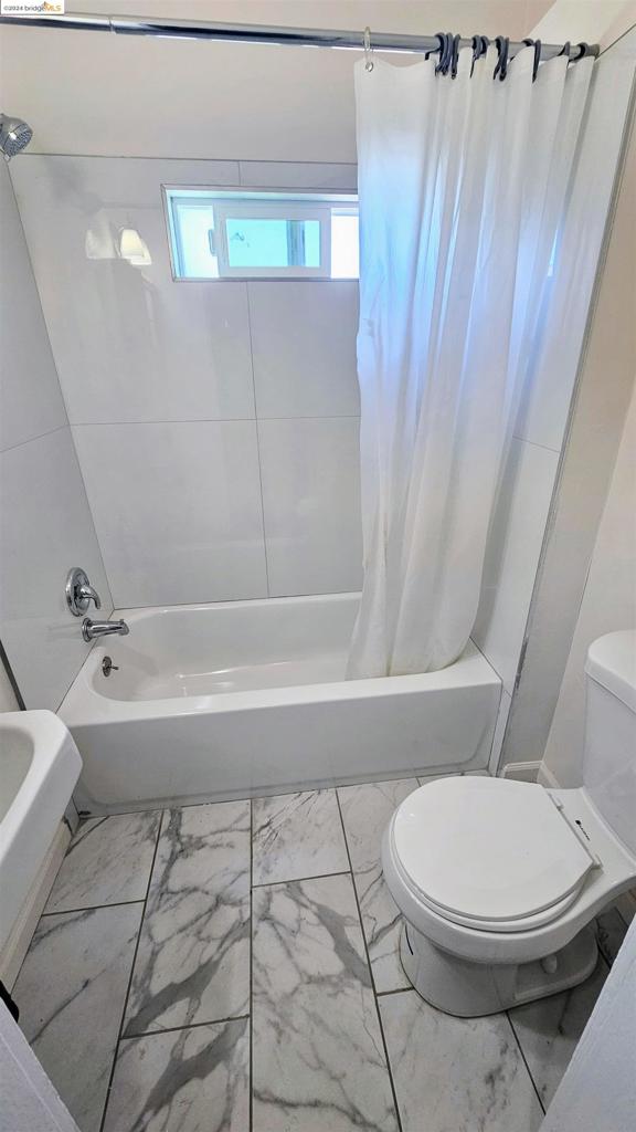 bathroom featuring shower / bathtub combination with curtain and toilet