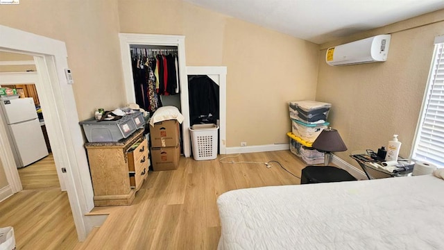 bedroom featuring white refrigerator, a closet, light hardwood / wood-style floors, and an AC wall unit