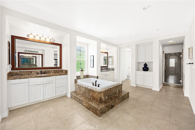 bathroom with a relaxing tiled tub, tile patterned flooring, vanity, and toilet