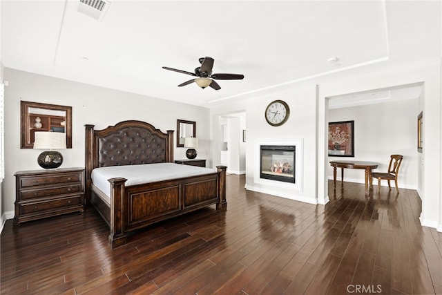 bedroom featuring ceiling fan, a multi sided fireplace, and dark hardwood / wood-style floors