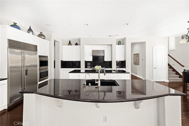 kitchen with sink, a large island with sink, dark wood-type flooring, white cabinetry, and stainless steel appliances