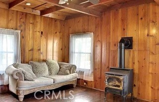 living room featuring dark wood-type flooring, a wood stove, beam ceiling, wooden walls, and wooden ceiling