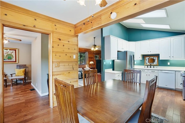 dining area with ceiling fan, wood walls, light hardwood / wood-style floors, and vaulted ceiling with skylight