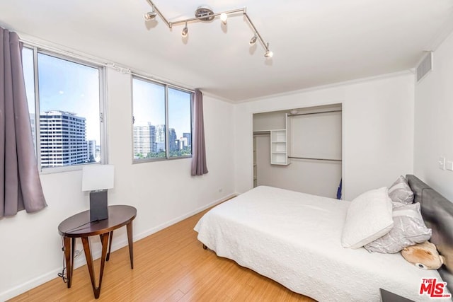 bedroom featuring wood-type flooring, multiple windows, a closet, and ornamental molding