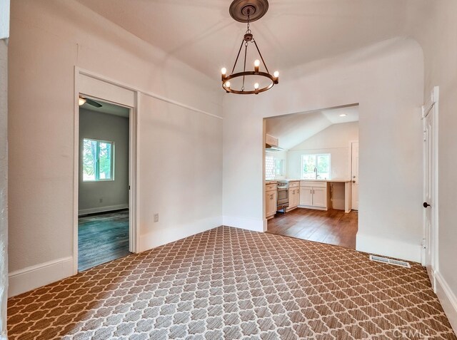 unfurnished room featuring a wealth of natural light, vaulted ceiling, a notable chandelier, and hardwood / wood-style flooring