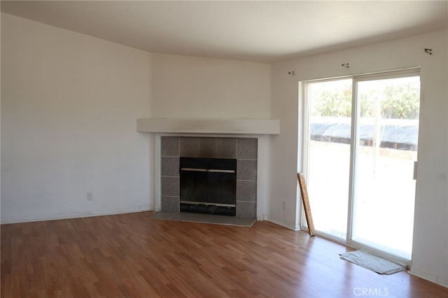 unfurnished living room with a tiled fireplace and wood-type flooring