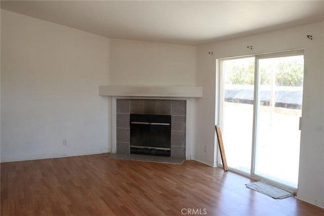 unfurnished living room featuring baseboards, a tile fireplace, wood finished floors, and a wealth of natural light