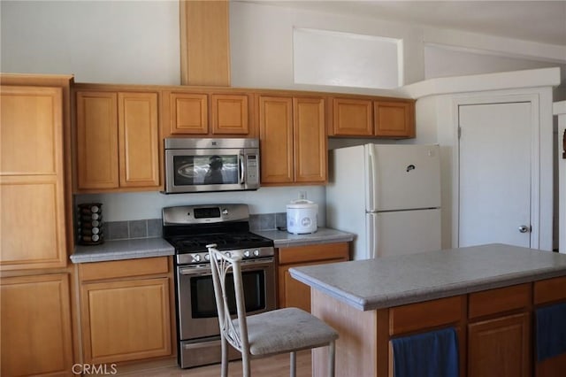 kitchen with brown cabinetry, vaulted ceiling, light countertops, and appliances with stainless steel finishes