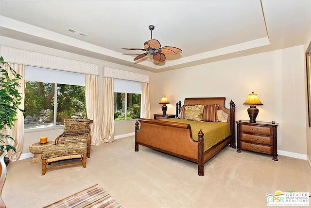 carpeted bedroom featuring multiple windows, a raised ceiling, and ceiling fan