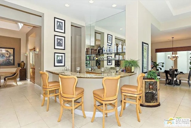 bar featuring light tile patterned floors, light stone countertops, and pendant lighting