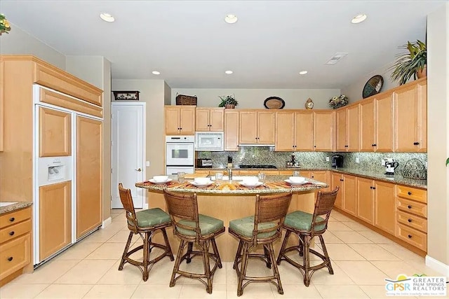 kitchen with light brown cabinets, light tile patterned floors, white appliances, tasteful backsplash, and light stone countertops