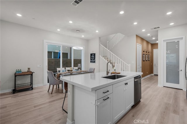 kitchen with sink, an island with sink, white cabinets, light hardwood / wood-style flooring, and stainless steel dishwasher