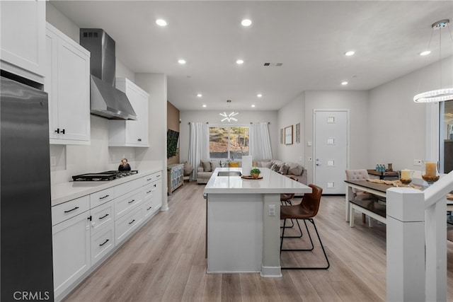 kitchen featuring white cabinets, light hardwood / wood-style flooring, wall chimney range hood, and a kitchen island