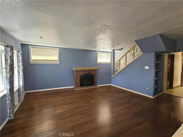 unfurnished living room with a textured ceiling, dark hardwood / wood-style flooring, a brick fireplace, and plenty of natural light