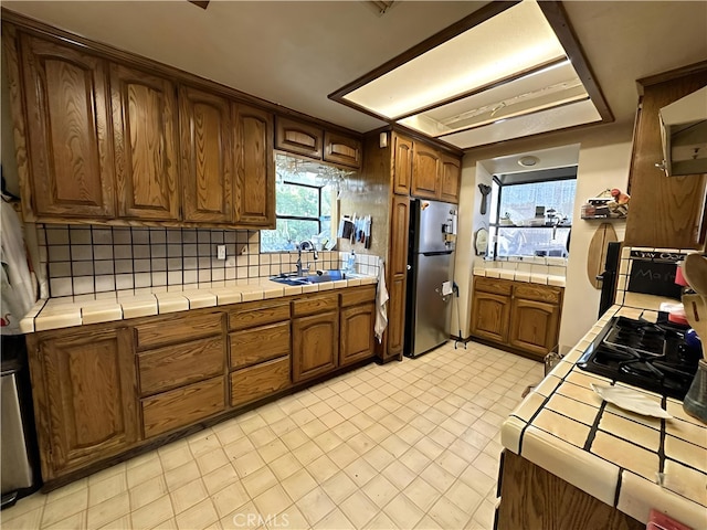 kitchen featuring tile countertops, white refrigerator, sink, decorative backsplash, and stainless steel fridge