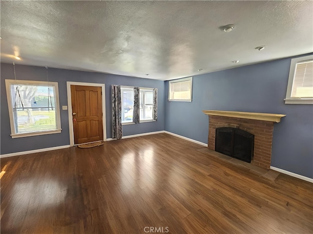 unfurnished living room featuring hardwood / wood-style floors, a textured ceiling, a brick fireplace, and plenty of natural light