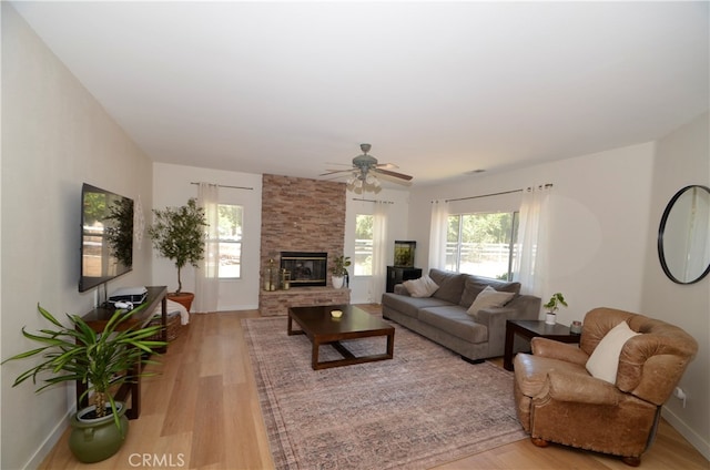 living room featuring light wood-type flooring, a stone fireplace, and ceiling fan