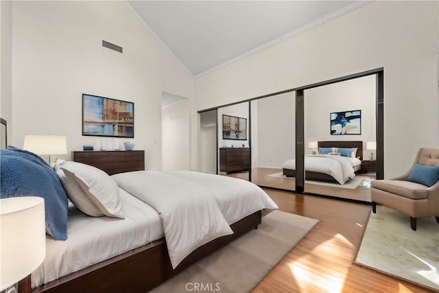 bedroom with a closet, hardwood / wood-style floors, high vaulted ceiling, and crown molding