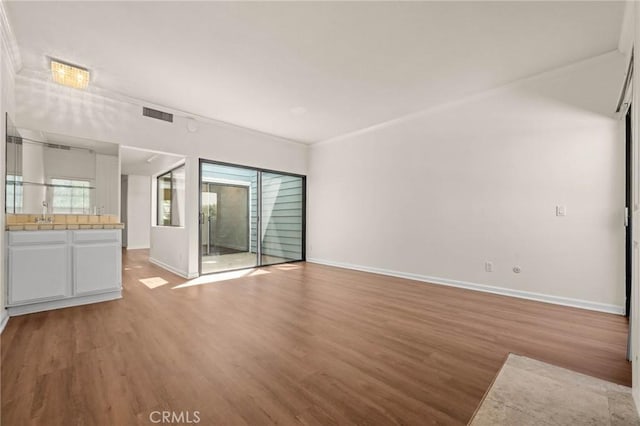 unfurnished living room featuring sink, wood-type flooring, and ornamental molding