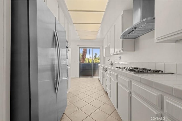 kitchen featuring light tile patterned flooring, white cabinetry, wall chimney exhaust hood, and stainless steel appliances