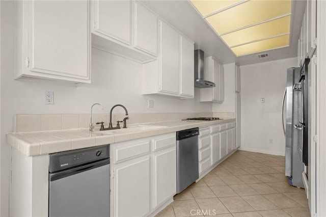 kitchen featuring white cabinetry, sink, wall chimney range hood, tile countertops, and appliances with stainless steel finishes