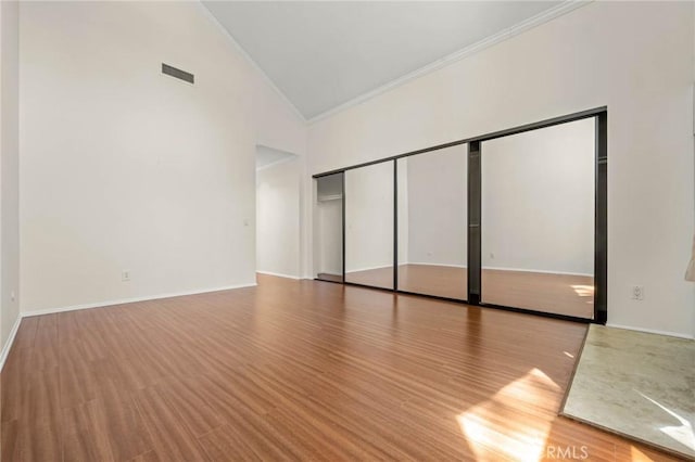 unfurnished bedroom featuring hardwood / wood-style floors, high vaulted ceiling, a closet, and crown molding