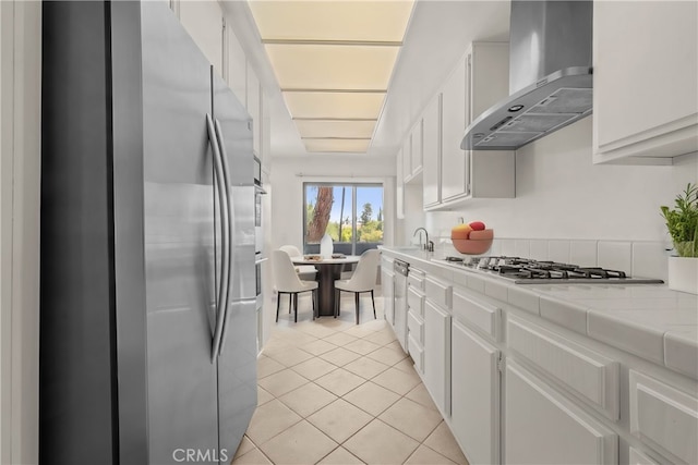 kitchen with white cabinetry, tile counters, wall chimney exhaust hood, light tile patterned floors, and appliances with stainless steel finishes