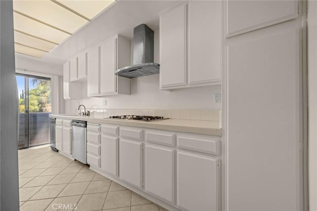 kitchen featuring white cabinets, stainless steel appliances, tile countertops, and wall chimney range hood