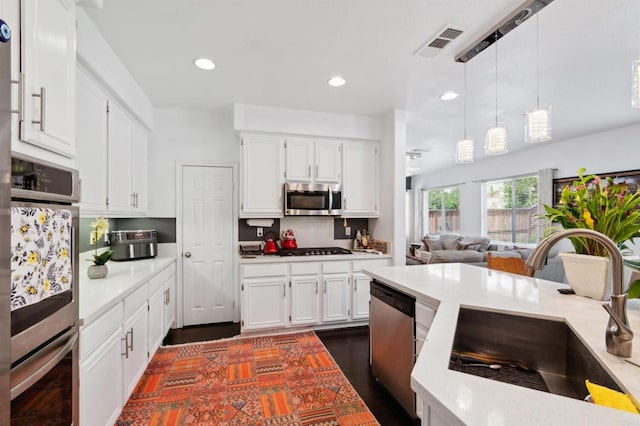 kitchen with appliances with stainless steel finishes, sink, white cabinetry, pendant lighting, and dark wood-type flooring