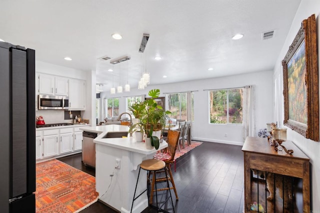 kitchen with a center island with sink, pendant lighting, white cabinetry, appliances with stainless steel finishes, and dark hardwood / wood-style flooring