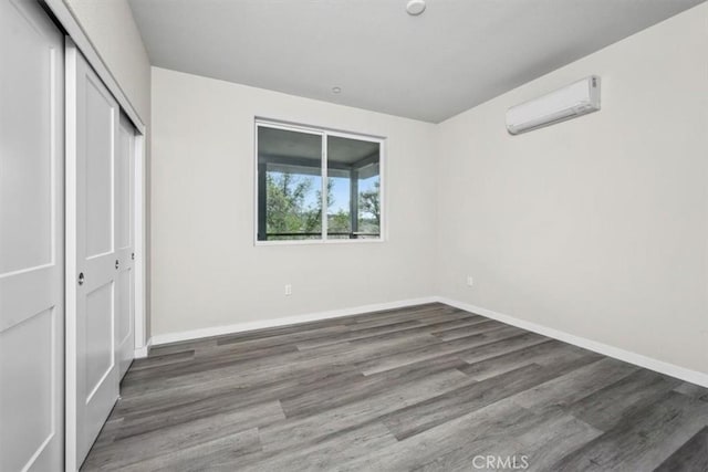 unfurnished bedroom with a closet, a wall mounted AC, and dark hardwood / wood-style floors