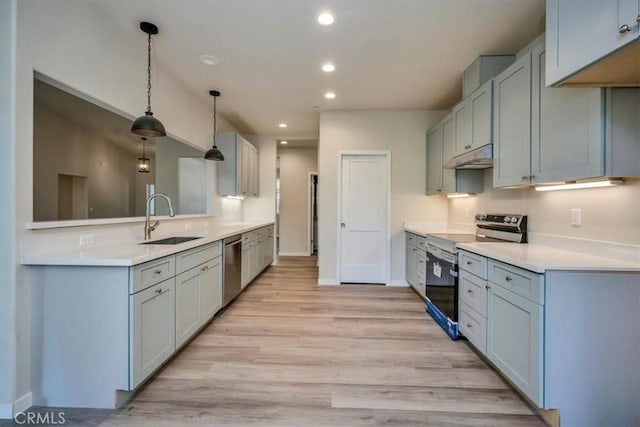 kitchen with light wood-type flooring, stainless steel appliances, hanging light fixtures, and sink