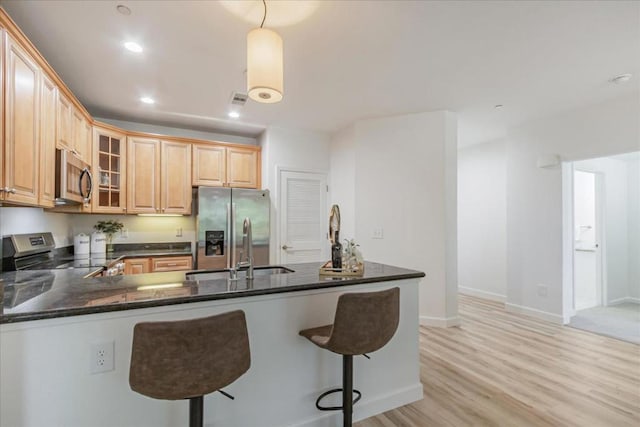 kitchen with decorative light fixtures, sink, kitchen peninsula, stainless steel appliances, and light hardwood / wood-style flooring