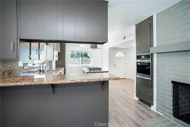 kitchen featuring gray cabinets, kitchen peninsula, oven, and light hardwood / wood-style floors