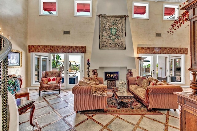 living room with a towering ceiling, a large fireplace, and french doors