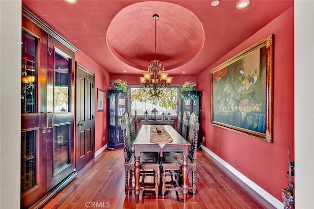 dining area with an inviting chandelier, a raised ceiling, and hardwood / wood-style floors