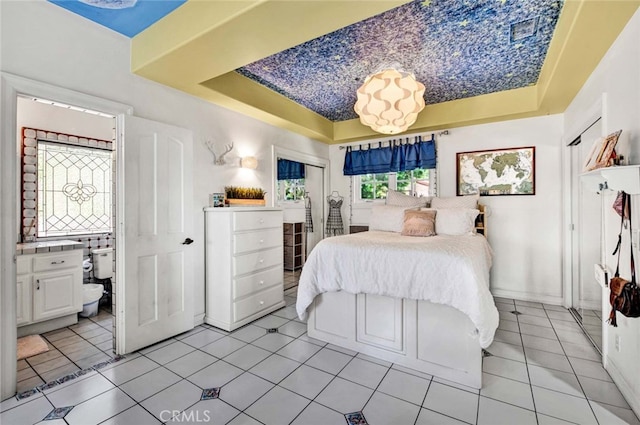 tiled bedroom with multiple windows, a raised ceiling, and ensuite bathroom