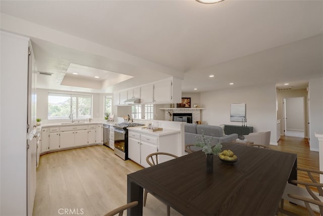 dining space with a fireplace, light hardwood / wood-style flooring, sink, and a tray ceiling