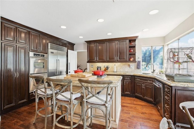 kitchen featuring sink, dark hardwood / wood-style floors, appliances with stainless steel finishes, tasteful backsplash, and light stone counters