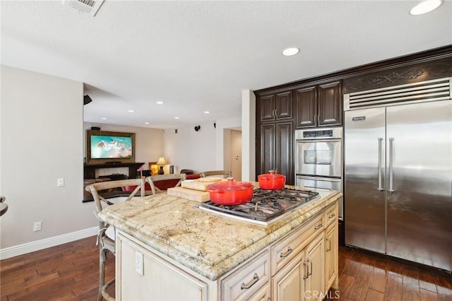 kitchen featuring stainless steel appliances, light stone counters, dark hardwood / wood-style floors, cream cabinetry, and a kitchen island