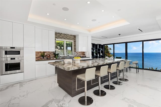 kitchen featuring double oven, a water view, a raised ceiling, and a spacious island