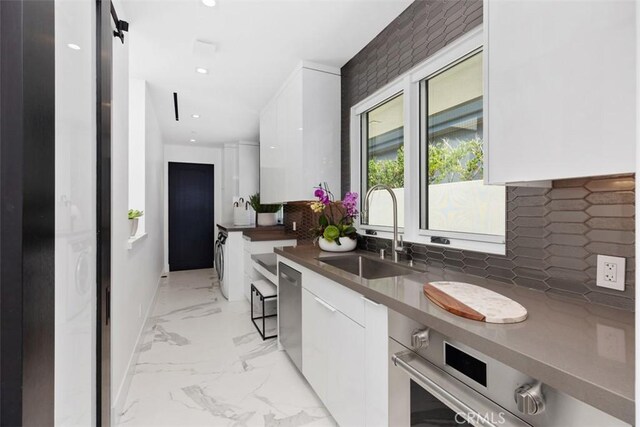 kitchen featuring sink, white cabinetry, dishwasher, a barn door, and decorative backsplash